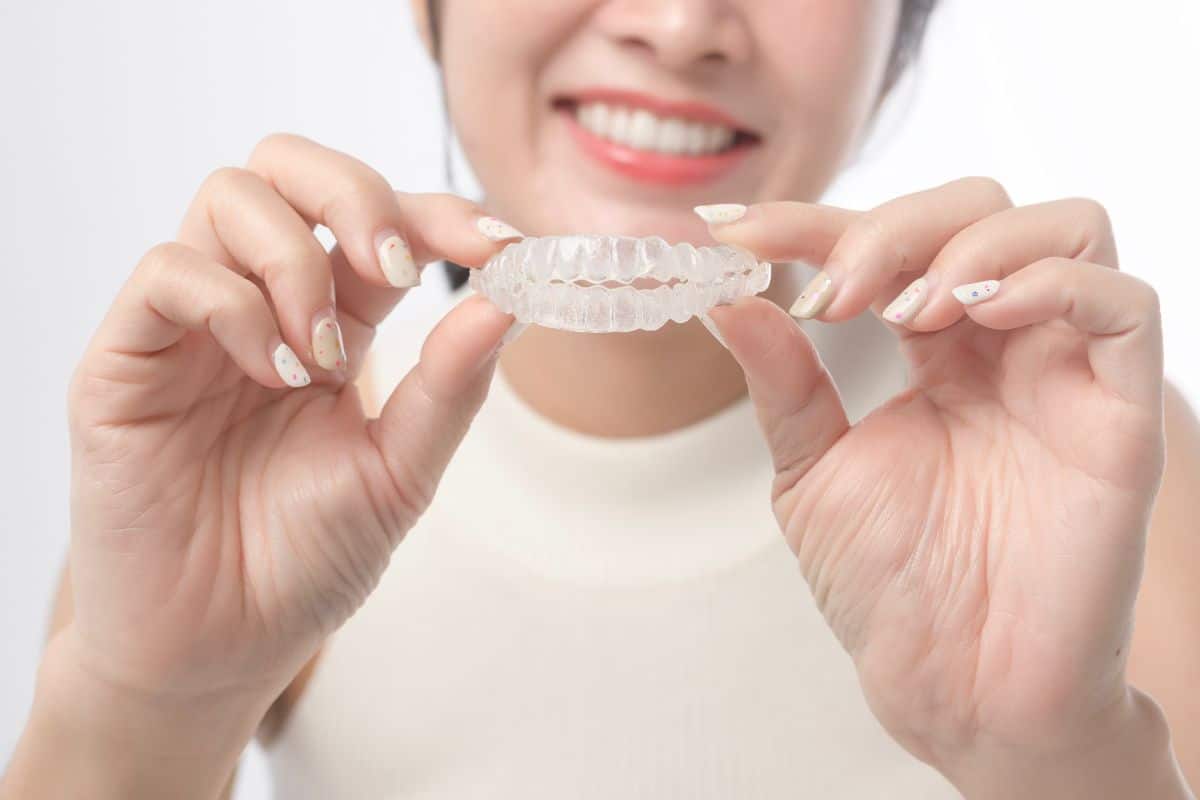 A woman holding a clear Invisalign aligner and smiling.
