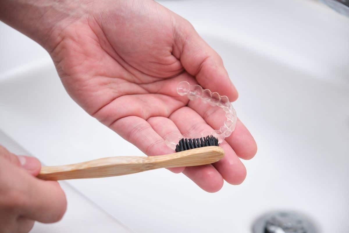 Person cleaning Invisalign aligners with a soft brush.