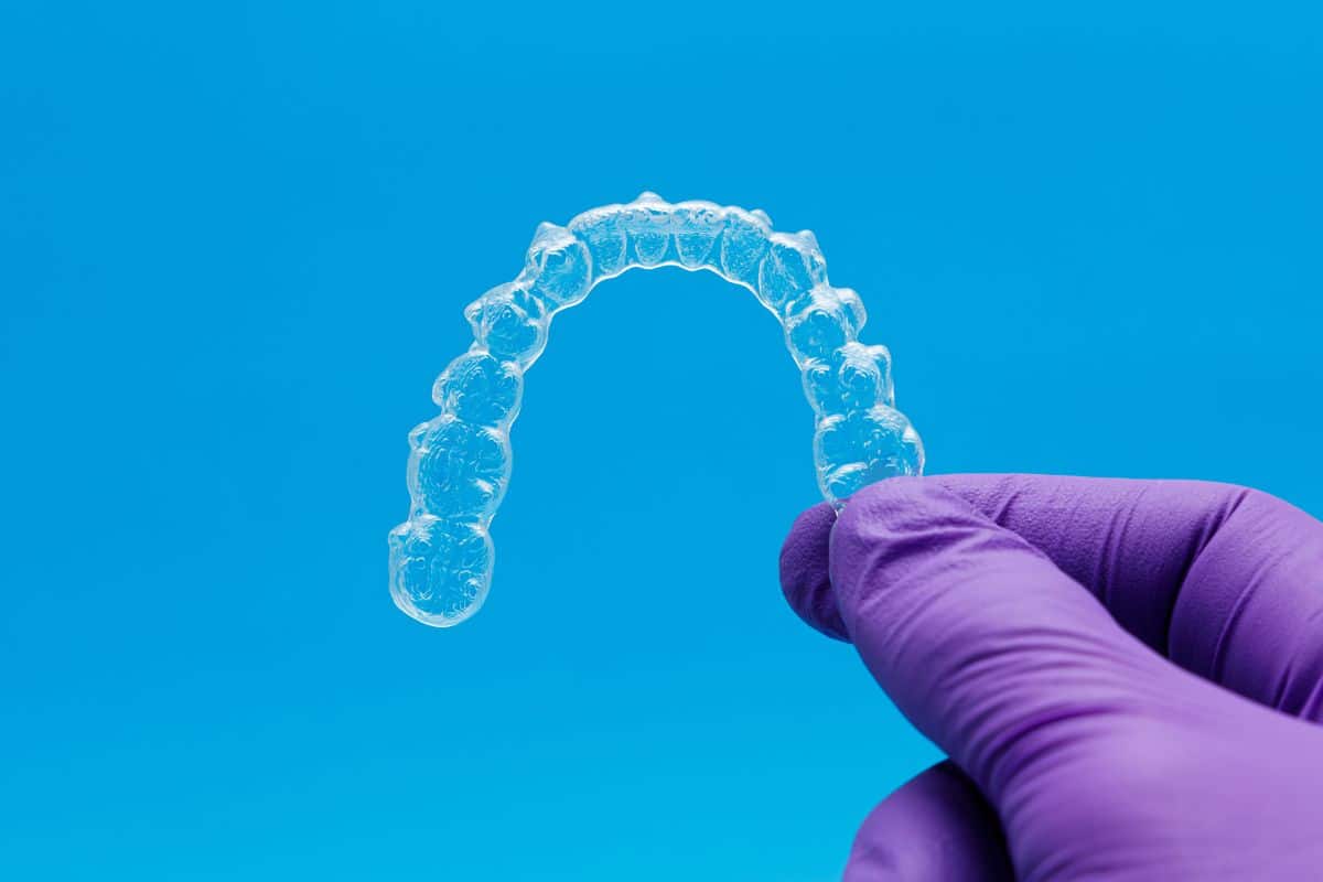 Clear Invisalign aligner held by a dental professional symbolizing a discreet path to improved confidence and mental well-being.