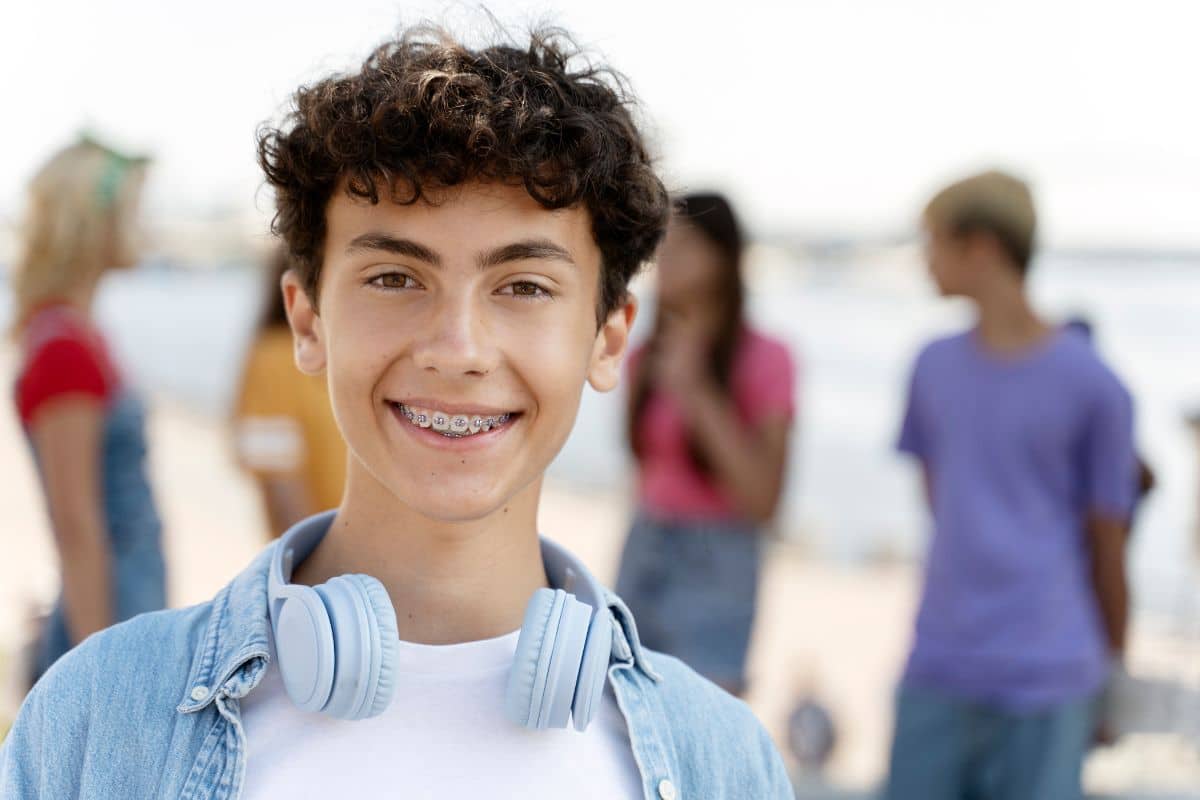 Teen smiling with braces outdoors during summer, highlighting healthy orthodontic care and confidence.