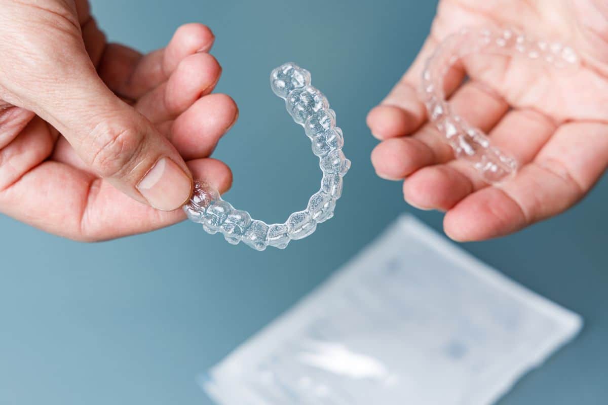 Hands holding clear Invisalign aligners.